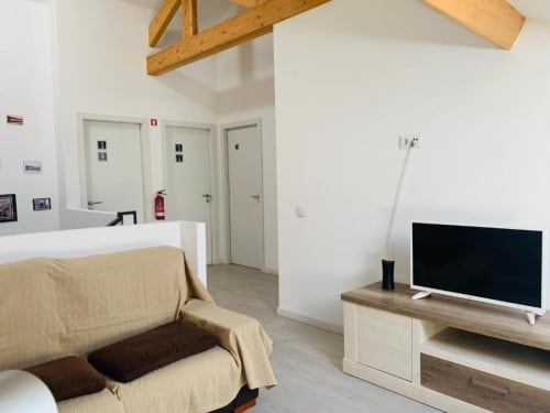 Modern studio room at Campanhã Boutique Station in Porto with beige sofa, TV, wooden ceiling beams, and three doors leading