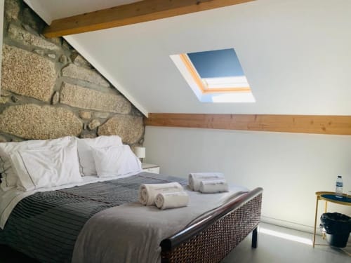 Modern attic bedroom at Campanhã Boutique Station in Porto with exposed stone wall, skylight, wooden beams, and rolled towels