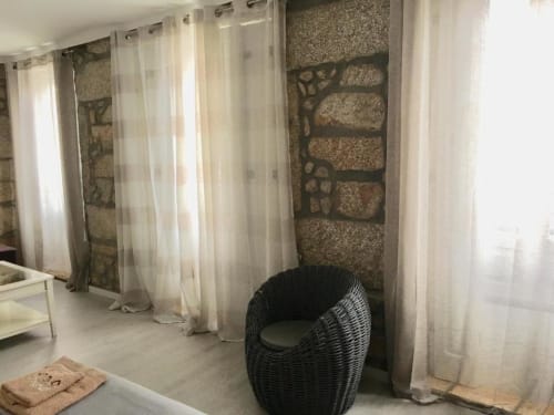 Quarto moderno na Estação Boutique Campanhã Porto com cadeira de vime, cortinas translúcidas, parede de pedra texturizada e design contemporâneo
