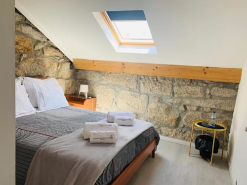 Attic bedroom at Campanhã Boutique Station Porto with stone walls, skylight, wooden beam, bed with towels, and yellow side