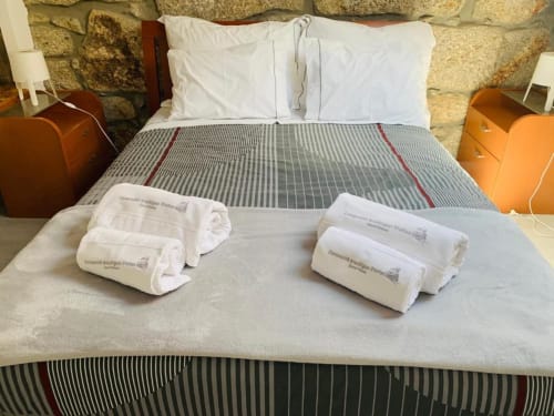 Bed with white pillows and striped blanket at Campanhã Boutique Station Porto, with rolled white towels displayed on foot.