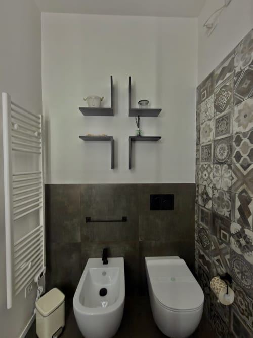 Bagno moderno nella Sibilla Suite di Manu Maison, Parma con bidet, wc, ripiani sospesi neri, piastrelle decorate e finiture bianche