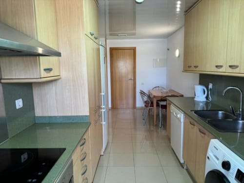 Modern kitchen in Salou apartment with light wood cabinets, green countertops, stainless steel appliances, and dining area