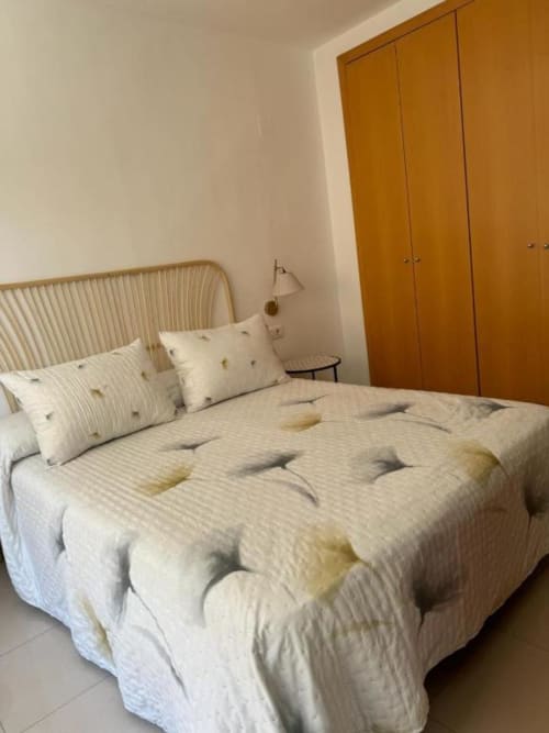 Modern bedroom in Salou apartment with striped bedding, wicker headboard, wooden wardrobe, and garden view