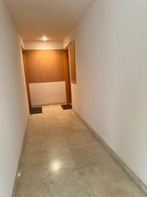 Empty hallway with tiled flooring and wooden doors in a Salou apartment, leading to rooms with white walls and recessed