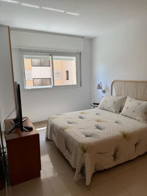 Bright bedroom in Salou apartment with queen bed, wooden headboard, flat-screen TV, and window with garden views