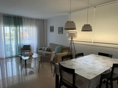 Modern 3-bedroom apartment in Salou with dining area, seating, pendant lighting, and garden view through glass doors