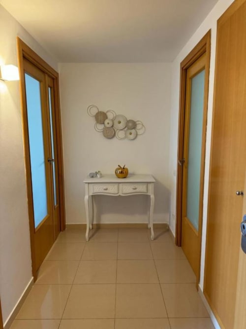 Elegant hallway in Salou apartment with cream tiles, wooden doors, white console table, and decorative wall art
