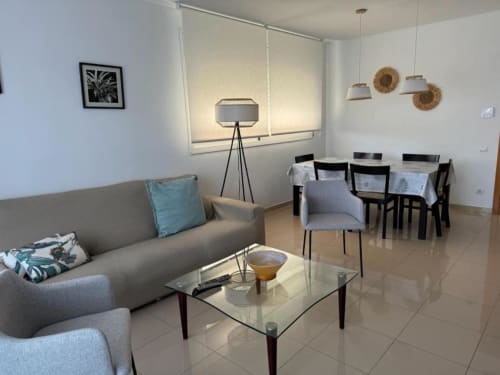 Modern 3-bedroom apartment living area in Salou with gray sofa, glass coffee table, dining area, and garden views