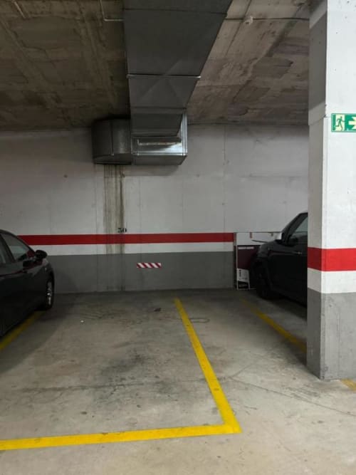 Underground parking garage at Rentalaya apartment in Salou with marked spaces, concrete columns, and exit sign