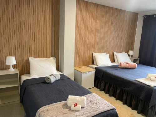 Chambre twin à la Liber Guest House de Braga avec lits noirs, oreillers blancs, murs en bois et équipements modernes