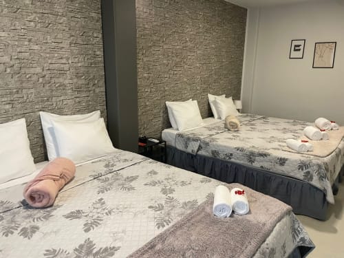 Chambre triple aux murs de briques à la Guest House Liber de Braga, avec serviettes roulées et oreillers blancs