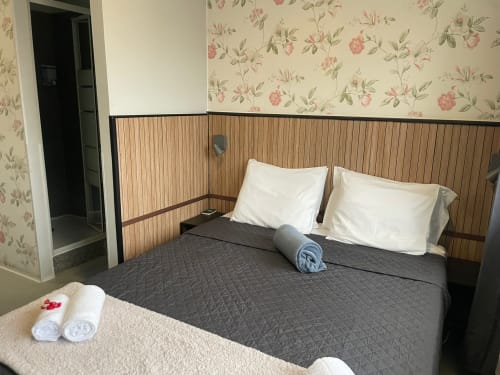 Quarto na Liber Guest House em Braga com papel de parede floral, cama de madeira, almofadas brancas e toalhas enroladas