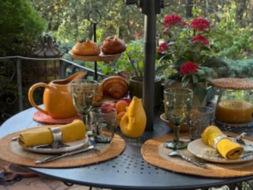 Table dressée dans le jardin de Lou Paradou Lodge avec serviettes jaunes, pichet orange et fleurs rouges à Grillon