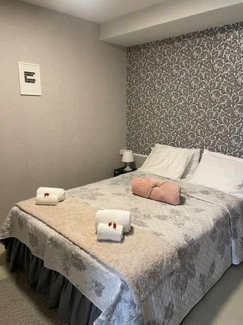 Quarto moderno na Liber Guest House em Braga com cabeceira estampada, roupa de cama branca e toalhas enroladas