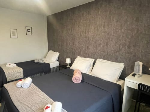 Chambre triple économique à la Liber Guest House à Braga avec deux lits, literie sombre, oreillers blancs, serviettes roulées et espaces partagés