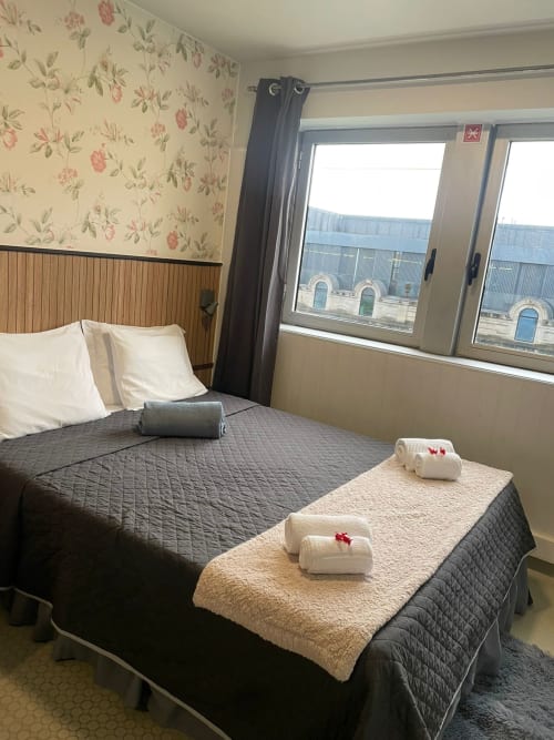 Chambre triple à la Liber Guest House à Braga avec papier peint floral, rideaux épais et fenêtres avec vue sur le jardin