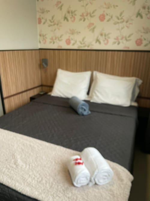Chambre triple confortable à la Liber Guest House Braga avec lit sombre, oreillers blancs et équipements