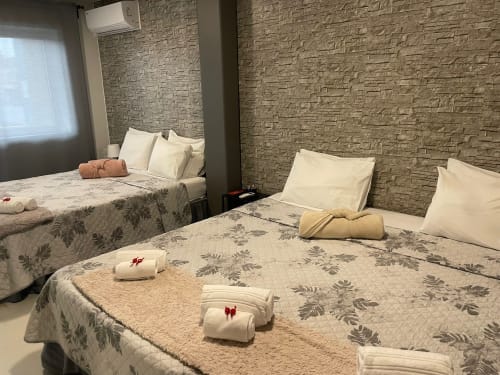 Plusieurs lits avec literie florale et oreillers blancs dans la chambre familiale de la Liber Guest House à Braga, avec murs en pierre