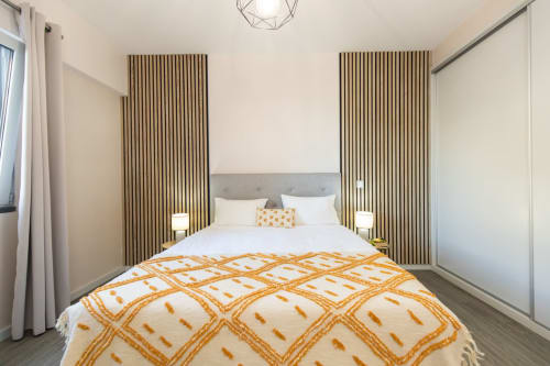 Quarto moderno no apartamento Rent-A-Key em Portugal com cama queen, almofadas douradas, painéis de madeira e design contemporâneo