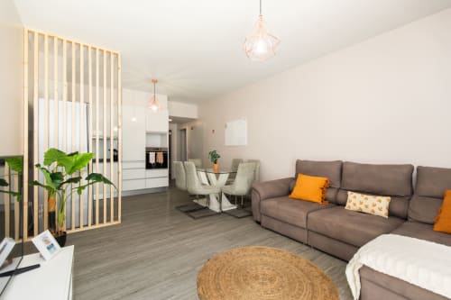 Sala de estar moderna com sofá marrom, área de jantar, cozinha, divisória em madeira e luminárias rose gold