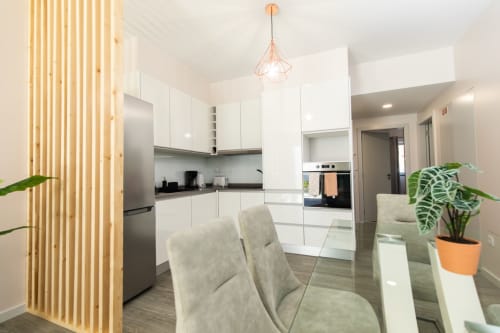 Cozinha e sala de jantar modernas no apartamento Rent-A-Key com armários brancos, parede de madeira e plantas verdes.