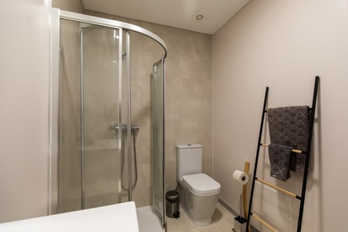 Banheiro moderno do apartamento Rent-A-Key com box de vidro, vaso sanitário e toalheiro aquecido com design de escada preta.