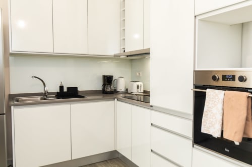 Cozinha moderna branca com eletrodomésticos em aço inoxidável e bancada escura no apartamento Rent-A-Key, Portugal