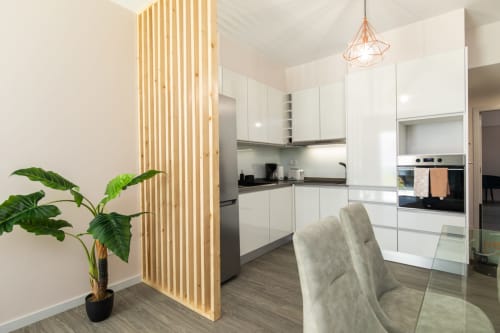 Cozinha moderna com armários brancos, divisória de madeira, planta em vaso e cadeiras cinza de jantar no apartamento Rent-A-Key