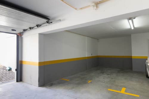 Garagem de estacionamento vazia com marcações de segurança amarelas e paredes listradas no apartamento Rent-A-Key em Portugal