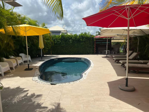 Espace piscine du Domaine De Marly à Sainte-Anne avec chaises longues, parasols et décor tropical