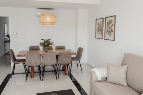 Modern dining area in Baeza apartment with wooden table, upholstered chairs, pendant light, and living room seating