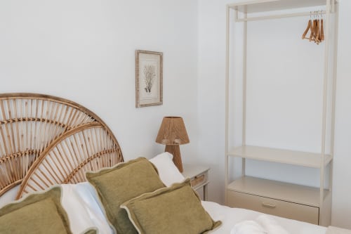 Bedroom with rattan chair, green pillows, wooden wardrobe, and framed botanical art at Alojamientos Estrella Baeza, Baeza