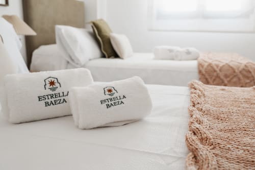 Estrella Baeza hotel apartment bed with branded towels and beige knit blanket in Baeza