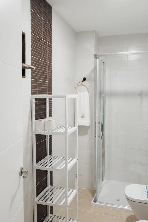 Modern bathroom with white shelving, dark tile accent wall, glass shower enclosure, and toilet at Alojamientos Estrella