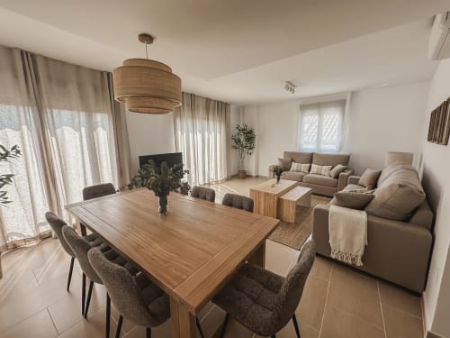 Modern open-plan living room with dining table, beige sofa, wooden pendant light, and mountain views at Alojamientos Estrella