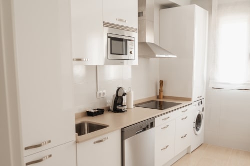 Modern white kitchen with built-in appliances, stainless steel sink, and washing machine in Baeza apartment