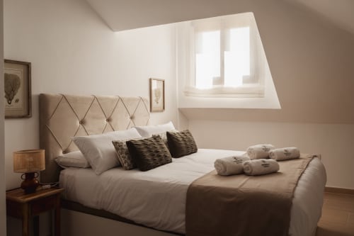 Bright attic bedroom at Alojamientos Estrella Baeza with quilted headboard, mountain views through skylights, and modern
