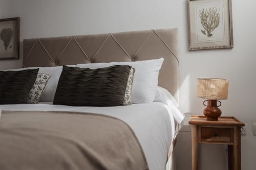 Elegant bedroom in Baeza apartment with beige quilted headboard, black and white pillows, wooden nightstand with woven lamp,