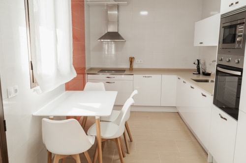 Modern apartment kitchen in Baeza with white cabinetry, dining table, stainless steel appliances and red tile accents