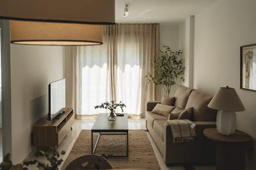 Modern living room with beige sofa, TV, mountain views through curtains at Alojamientos Estrella Baeza, Baeza