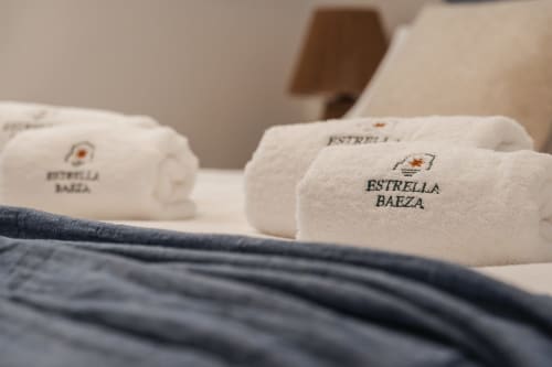 Luxury white towels embroidered with Estrella Baeza logo on a bed at Alojamientos Estrella Baeza hotel in Baeza, Spain