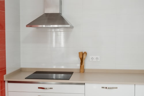 Modern kitchen corner with stainless steel range hood, white subway tiles, wooden utensil holder, and electrical outlets at