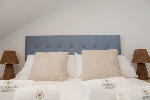 Bedroom at Estrella Baeza with blue upholstered headboard, beige pillows, white linens, and wooden bedside lamps