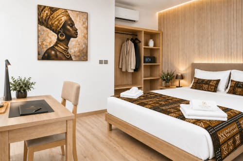 Modern bedroom at DakarByDays hotel in Dakar featuring African-inspired décor, wooden furnishings, and gold-toned artwork