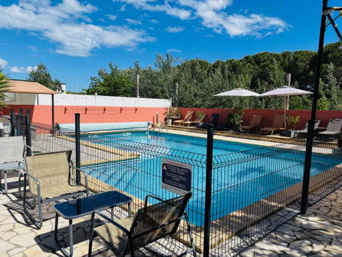 Swimmingpool des Gästehauses Entre 2 eaux in Marseillan-Plage mit Liegestühlen, Sonnenschirmen und grüner Umgebung unter blauem Himmel