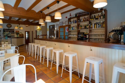 Interior del bar La Gerencia en Checa con vigas de madera, taburetes blancos y estantería de licores