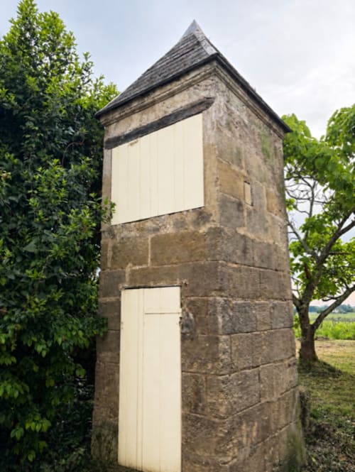Tour en pierre historique aux portes crème du Château Alto Cormeil à Saint-Émilion, entourée de lierre et d'arbres verdoyants