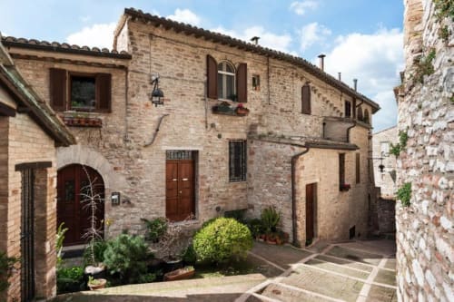Antico cortile in pietra dell'hotel Proprietà Clara ad Assisi, con porte in terracotta e piante in vaso