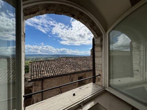 Vista dalla finestra di Proprietà Clara sugli tetti di Assisi e la campagna umbra con cielo azzurro